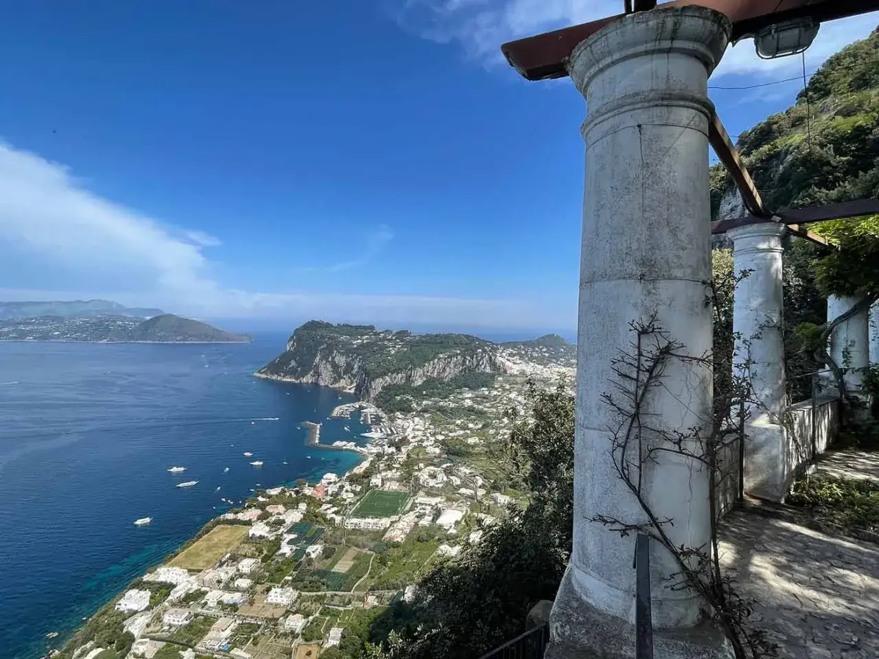 Un giorno a Capri: vista panoramica sul golfo, il porto e le case bianche, con colonne antiche in primo piano.