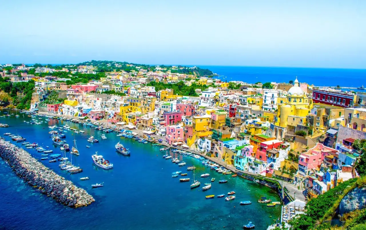 Coloratissima isoletta tra Napoli e Ischia, con case vivaci affacciate su un porto pieno di barche.