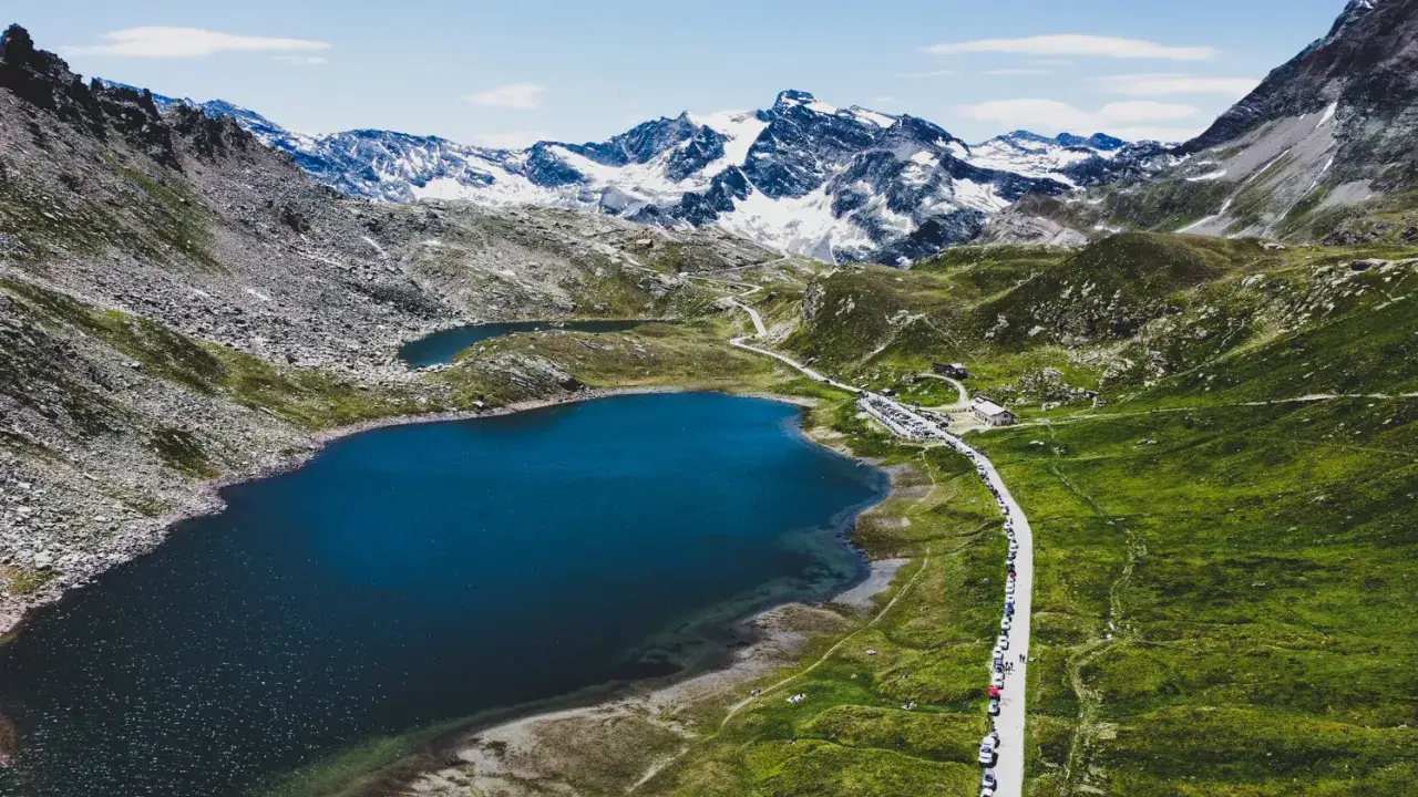 Laghi alpini e strada tortuosa sul colle del Nivolet, con montagne innevate sullo sfondo.