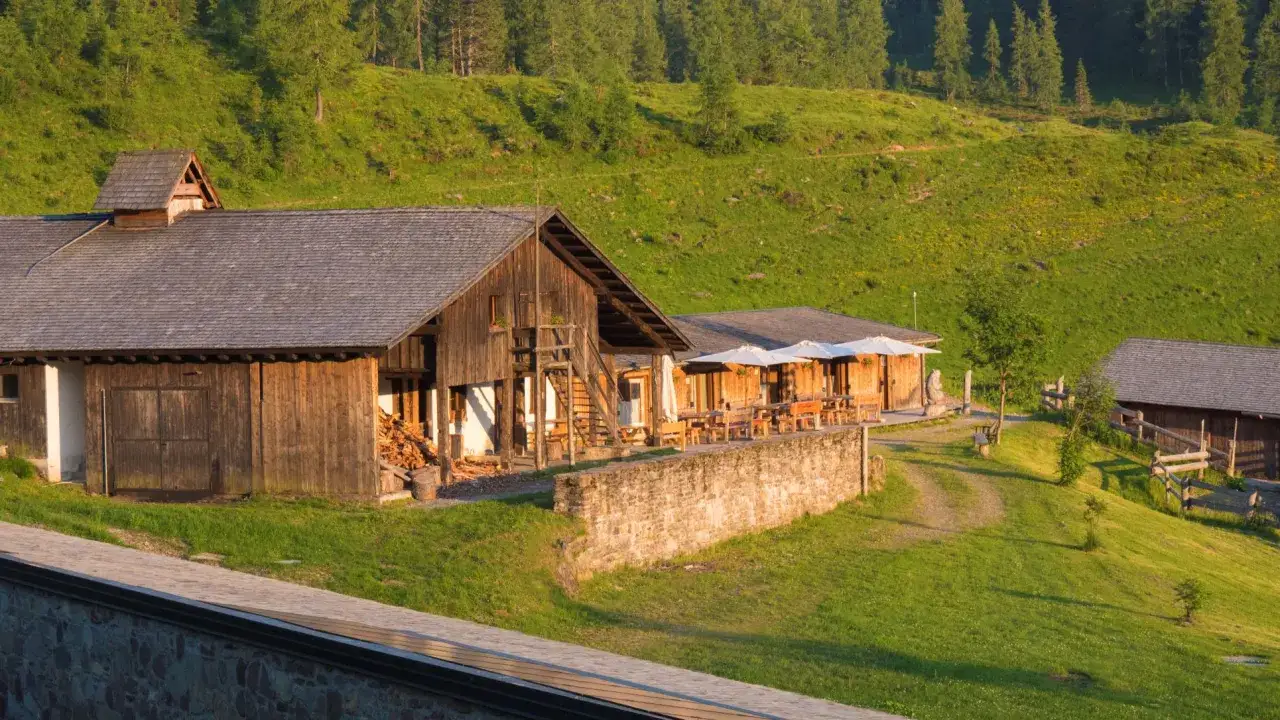 Malghe in Friuli: rustici edifici in legno con tavoli all'aperto, immersi nel verde di un prato fiorito e boschi.