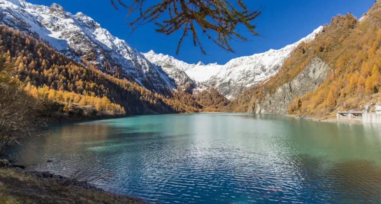 Lago alpino turchese circondato da montagne innevate e boschi autunnali dorati. Ideale per escursioni facili in Val d'Ossola.