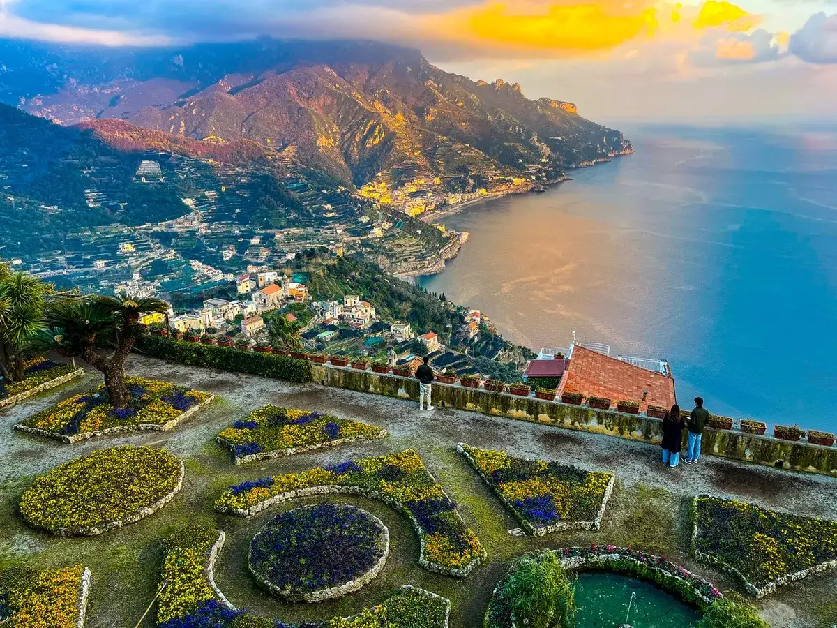 Giardini fioriti con vista mozzafiato sulla costa. Si ammira la distanza Ravello Amalfi, con il mare azzurro e le case aggrappate alla montagna.