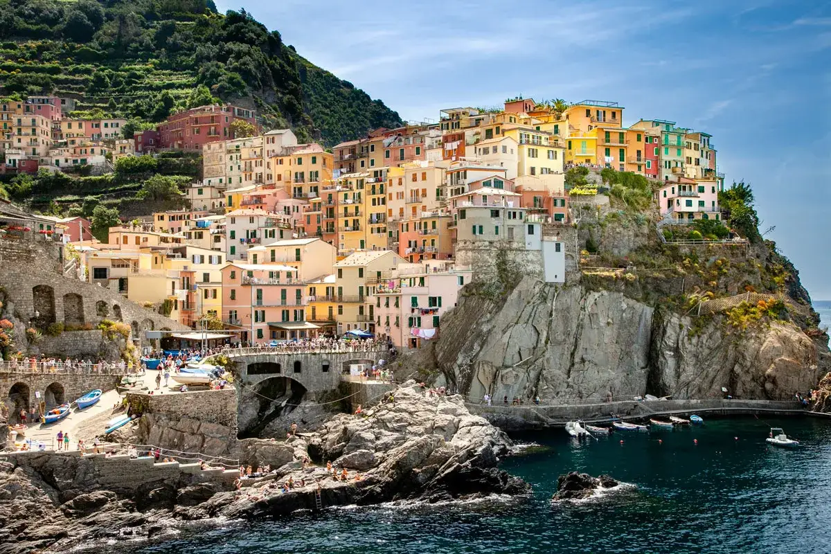 Case colorate aggrappate alla scogliera a picco sul mare, un gioiello delle Cinque Terre. Barche nel porticciolo, gente che si gode il sole.