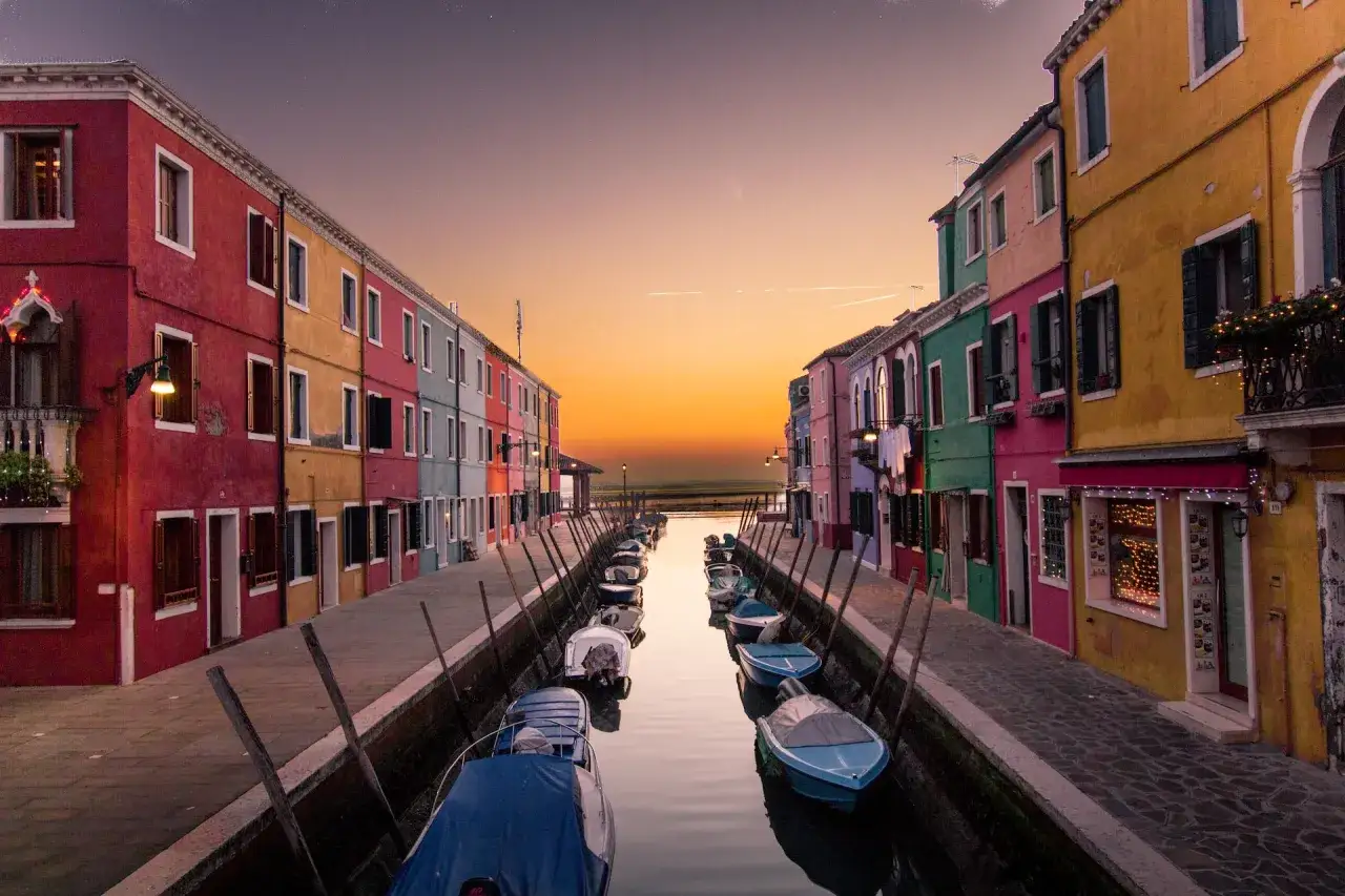 Colorate case affacciate su un canale con barche ormeggiate, al tramonto. Un'atmosfera magica tra Murano e Burano.