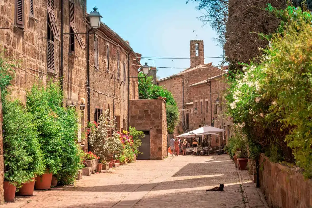 Un incantevole borgo toscano da visitare, con case in pietra, fiori colorati e un gatto che riposa al sole.