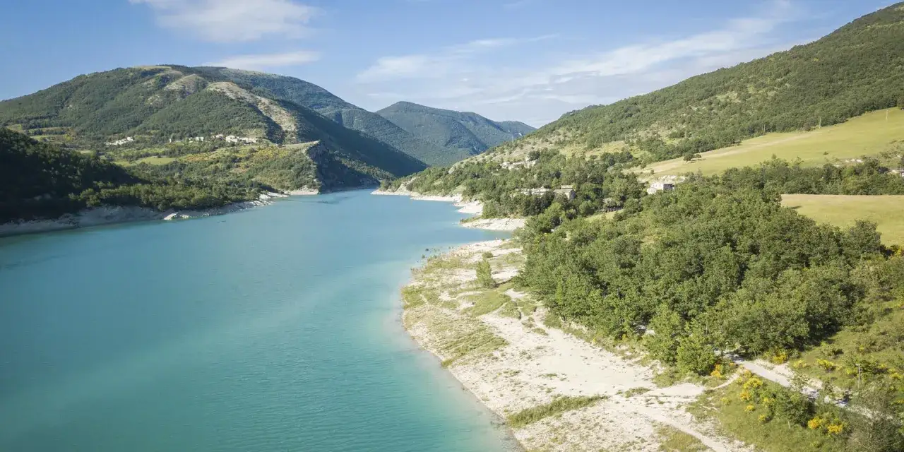 Il lago di Fiastra incanta con le sue acque turchesi, circondato da colline verdi e piccoli borghi.