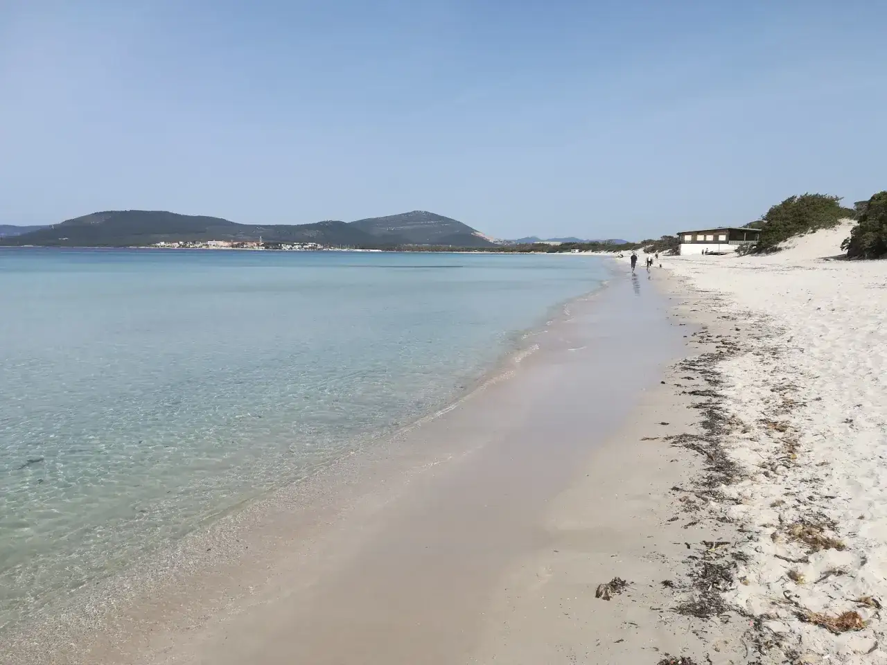 Passeggiata sulla spiaggia della Fertilia con mare cristallino e colline all'orizzonte.
