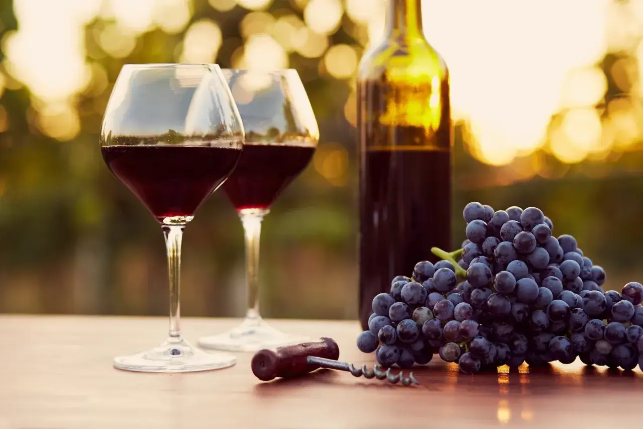 Calici di vino rosso, uva e cavatappi, perfetti per un tour enogastronomico in Toscana al tramonto.