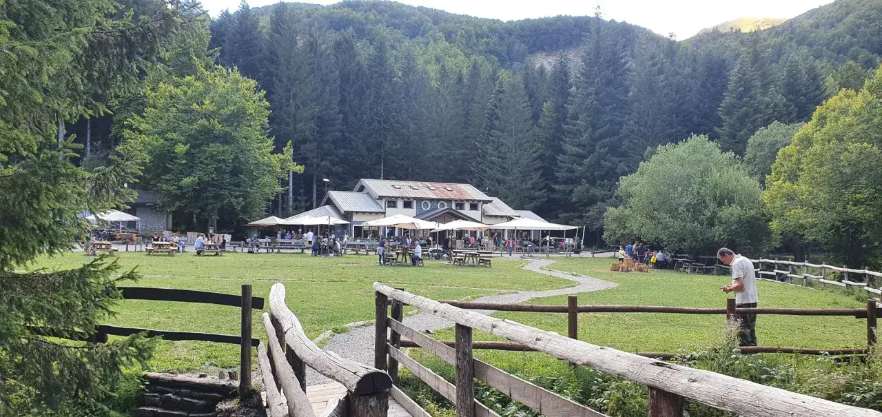 Un rifugio in Emilia Romagna immerso nel verde, con tavoli all'aperto e gente che si gode la giornata.