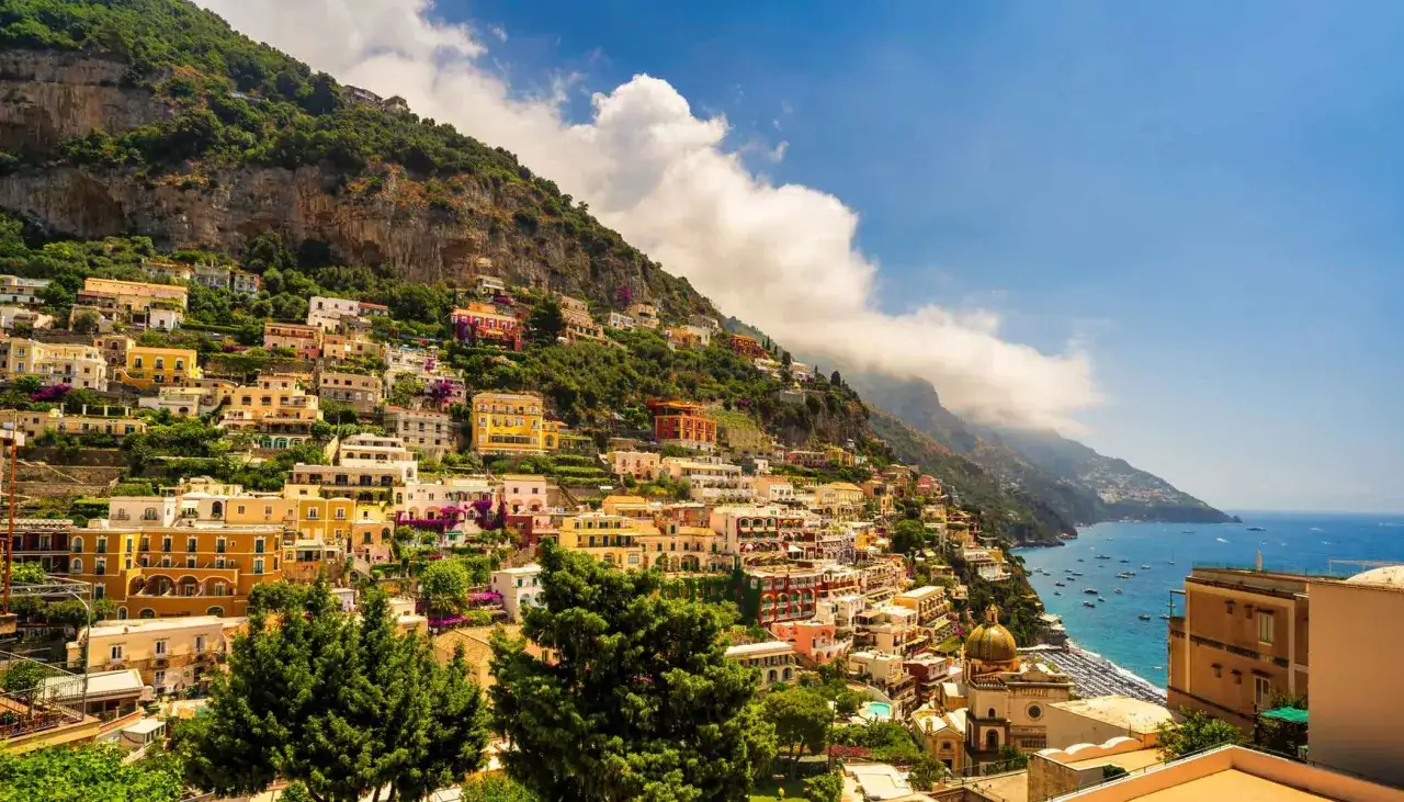 Case colorate aggrappate alla scogliera, un sogno per chi vuole visitare la Costiera Amalfitana senza auto, con il mare blu e le barche.