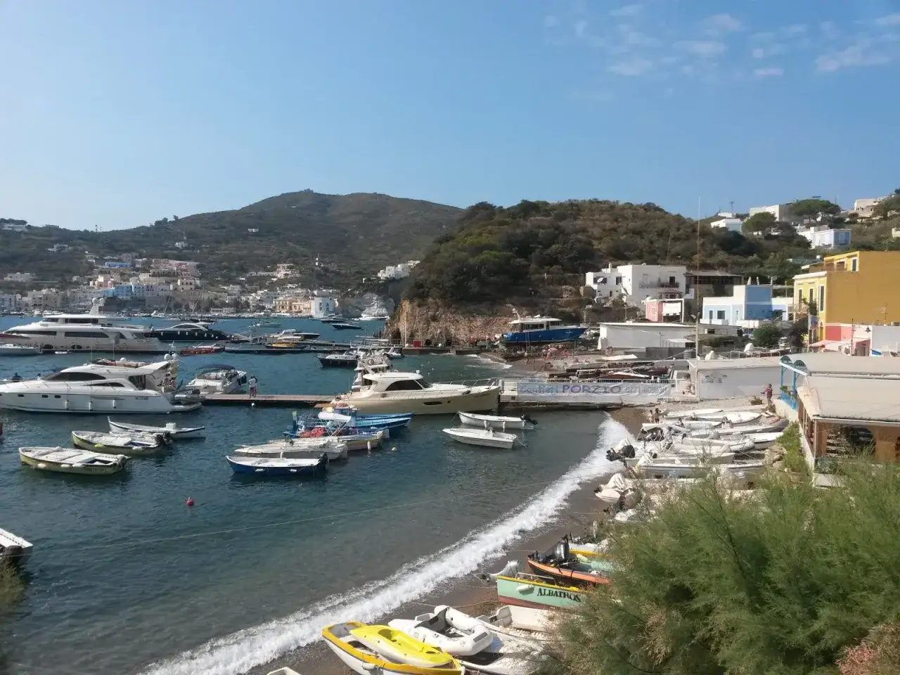 Porto di Santa Maria a Ponza, con yacht e barche ormeggiate, case colorate sulla collina e mare azzurro.