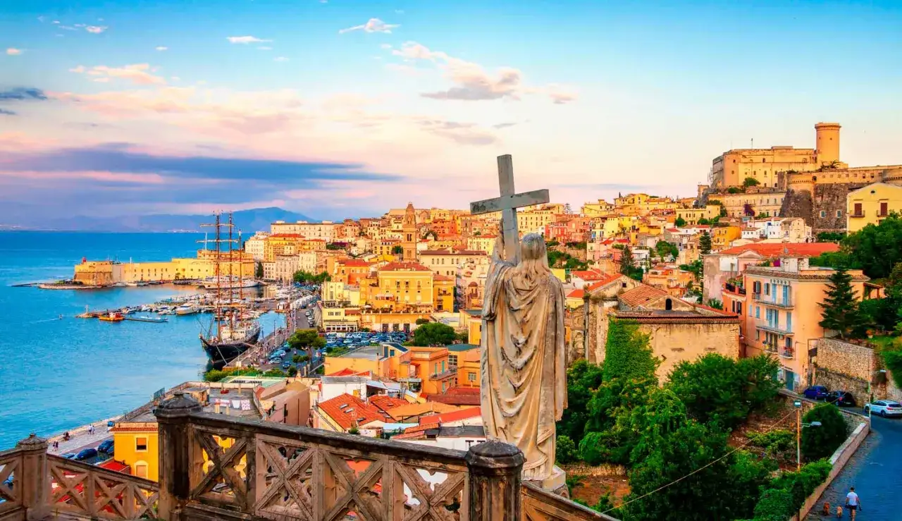 Statua con croce domina la vista di Gaeta, perfetta per una gita fuori porta da Roma. Porto, castello e case colorate al tramonto.