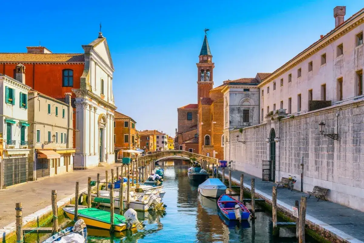 Un pittoresco canale nella città di mare veneto, con barche ormeggiate e antichi edifici che si specchiano nell'acqua.