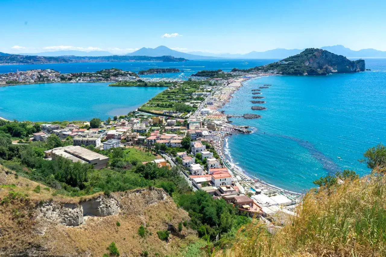Panoramica di una baia con acque turchesi, spiagge affollate e case colorate. Perfetto per scoprire cosa vedere a Procida in un giorno.