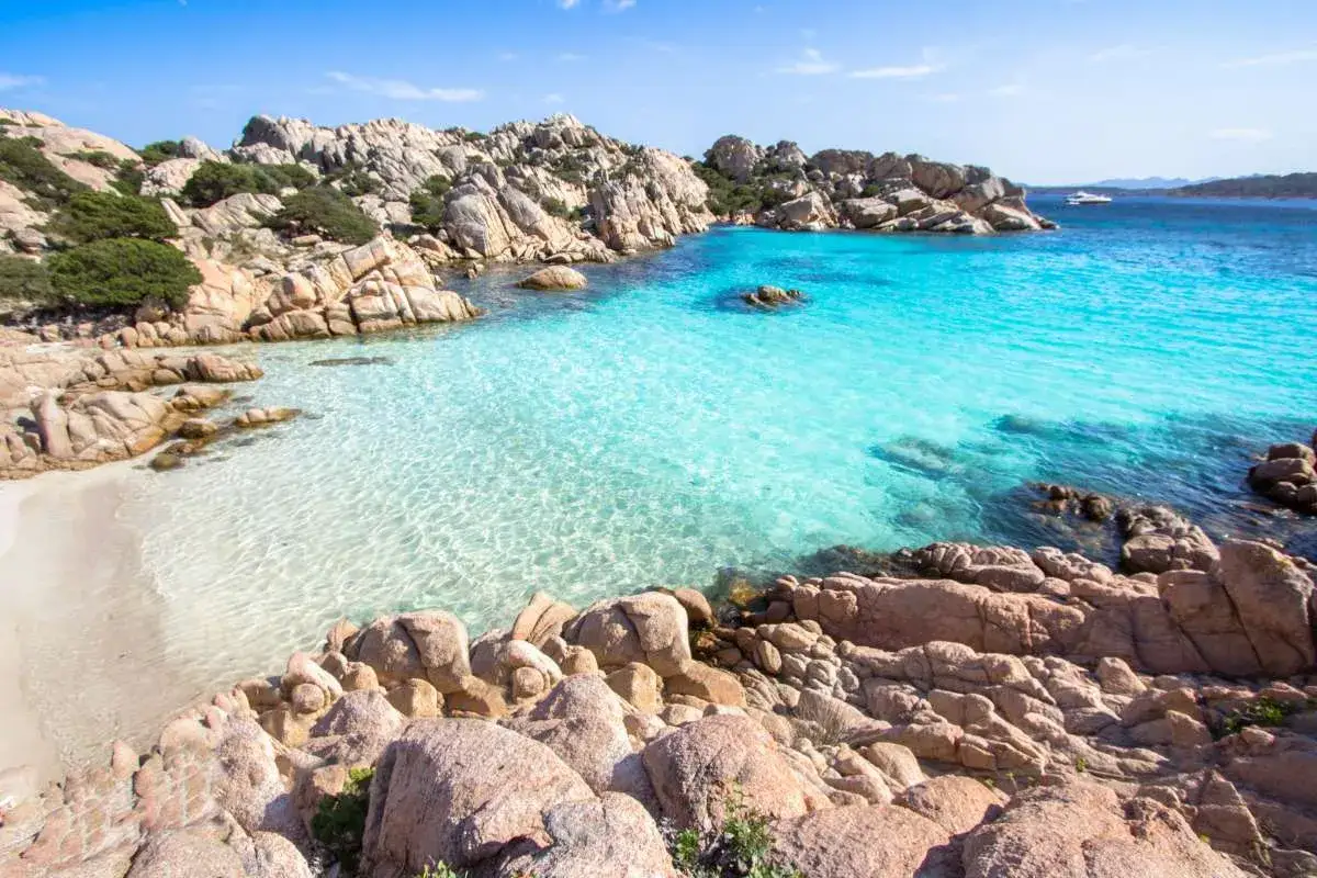 Spiaggia con rocce granitiche e mare cristallino, un angolo di paradiso che ricorda la bellezza di Sardegna e Sicilia.