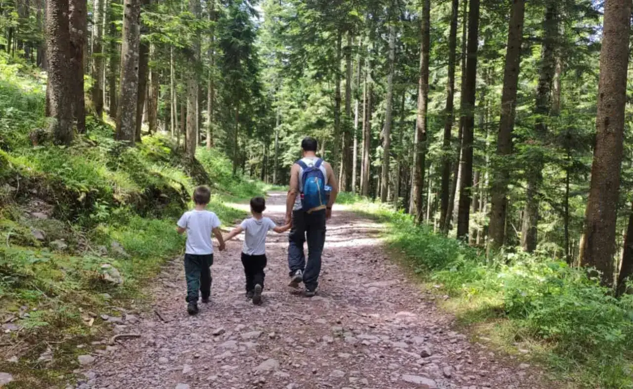 Un padre e i suoi due figli camminano su un sentiero nel bosco, godendosi le spiazzi di Gromo e le passeggiate nella natura.