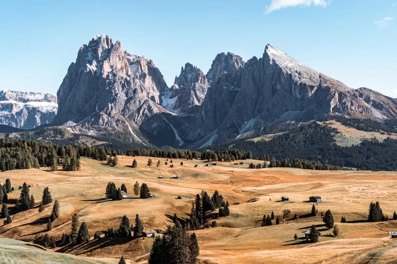 Altopiano con baite e boschi, ideale per capire dove andare in montagna in Trentino. Cime maestose sullo sfondo.