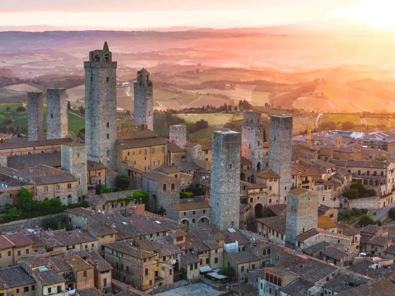 Torri medievali di San Gimignano, Siena, si stagliano contro un tramonto infuocato sulla campagna toscana.