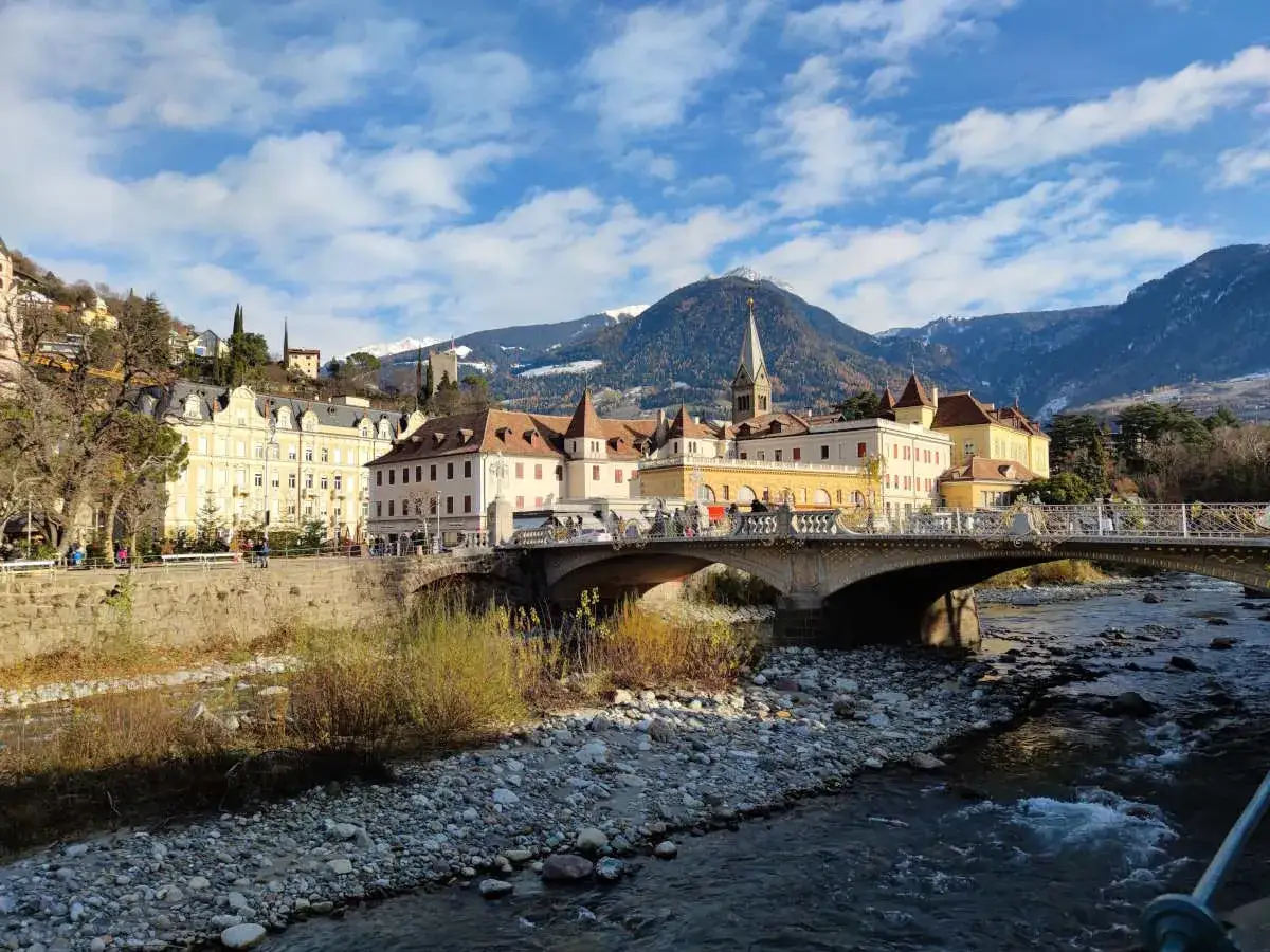 Ponte sul fiume Passirio a Merano, dove si trova questa incantevole cittadina alpina, con edifici storici e montagne innevate sullo sfondo.