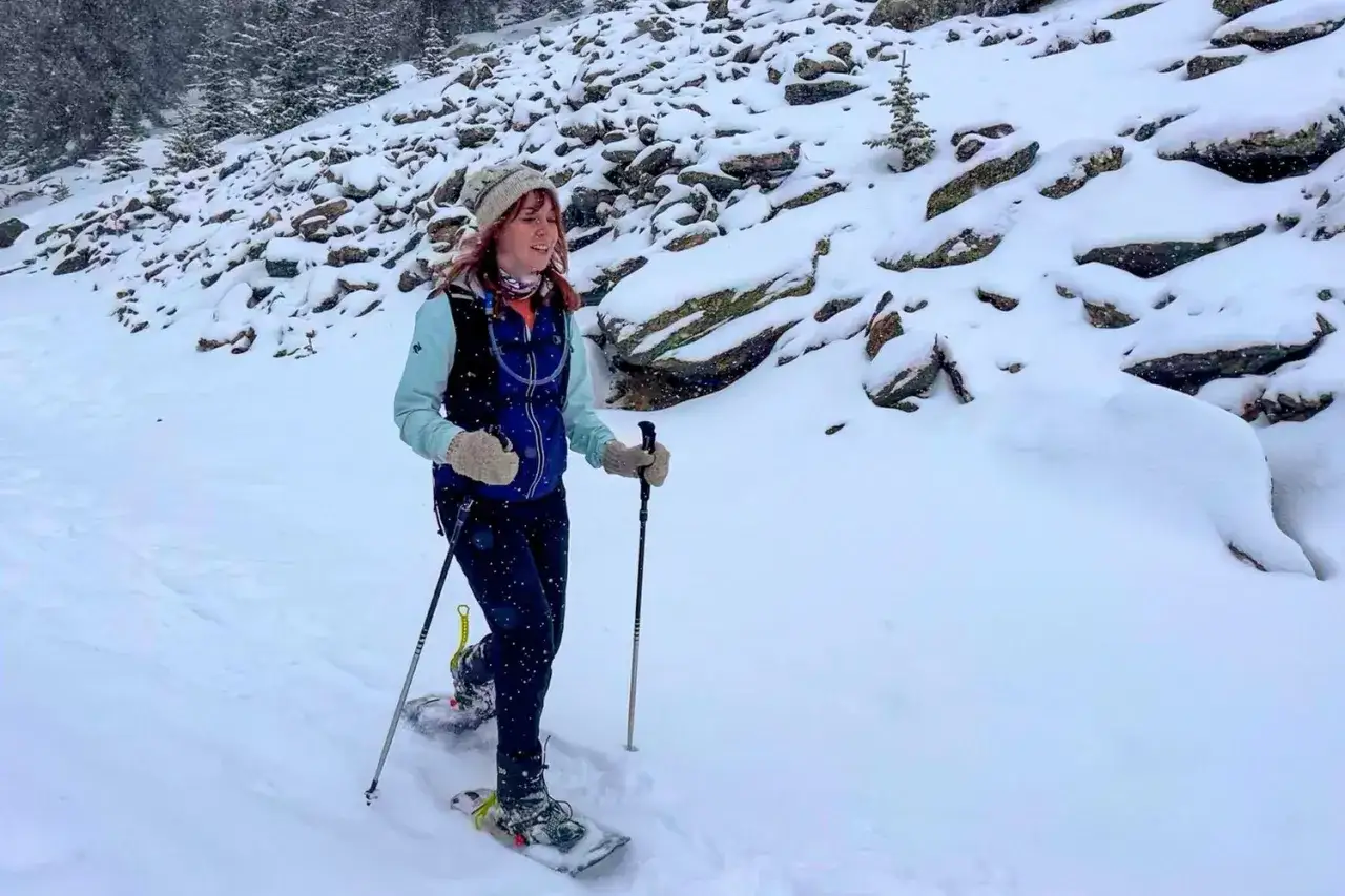 Donna con racchette da neve e bastoncini, godendosi le passeggiate sulla neve in un paesaggio innevato e roccioso.