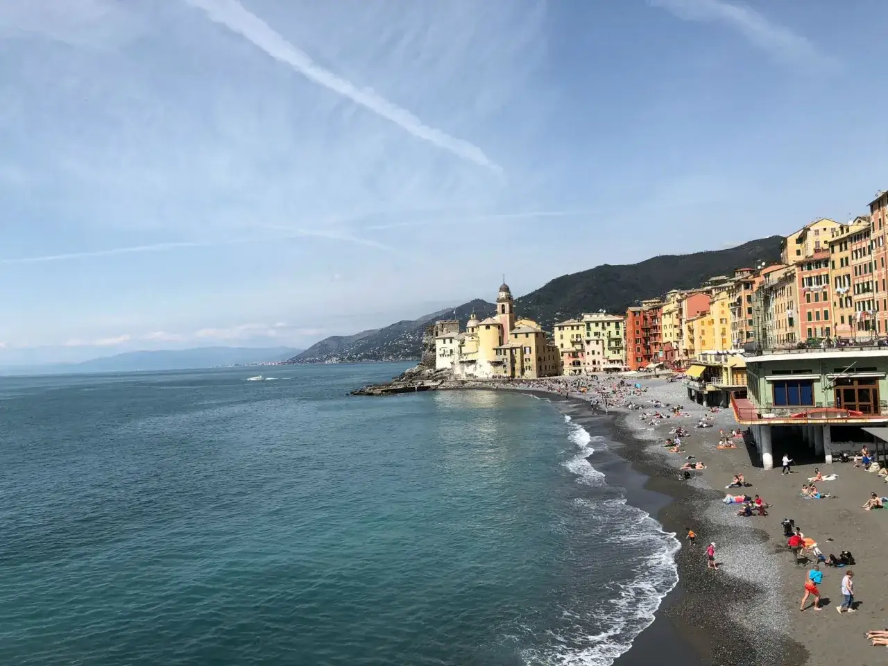 Camogli, il mare più vicino a Milano, con case colorate a picco sulla spiaggia affollata e il blu intenso del Mediterraneo.