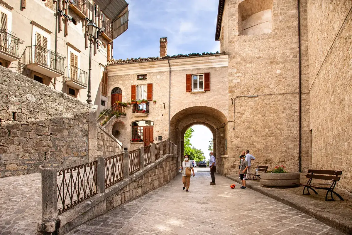 Un vicolo di Civitella del Tronto con case in pietra, un arco e persone che passeggiano.
