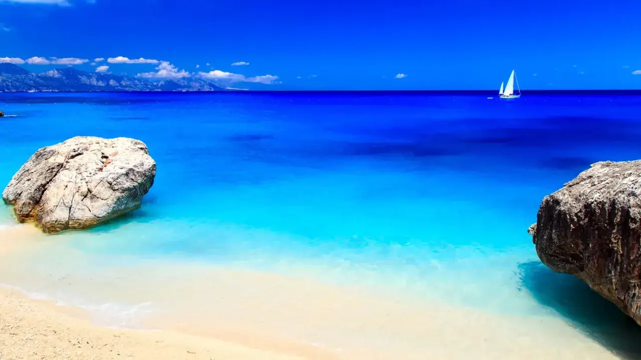 Spiagge più belle d'Italia: sabbia dorata, rocce scolpite dal mare e un veliero solitario solcano le acque cristalline di un paradiso.