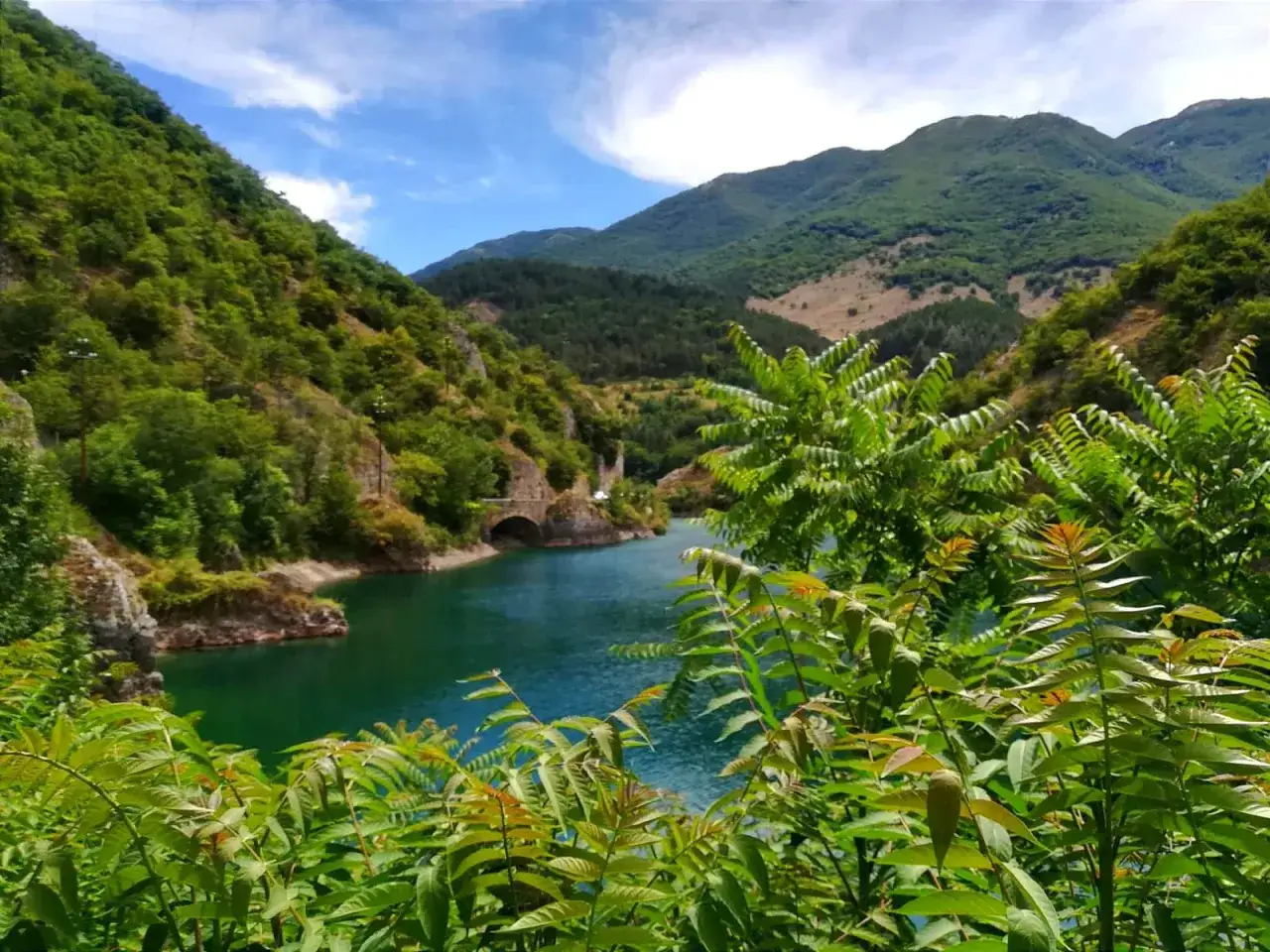 Un lago turchese incastonato tra montagne verdi, con un antico ponte ad arco. Un luogo da scoprire, un vero villalago cosa vedere.