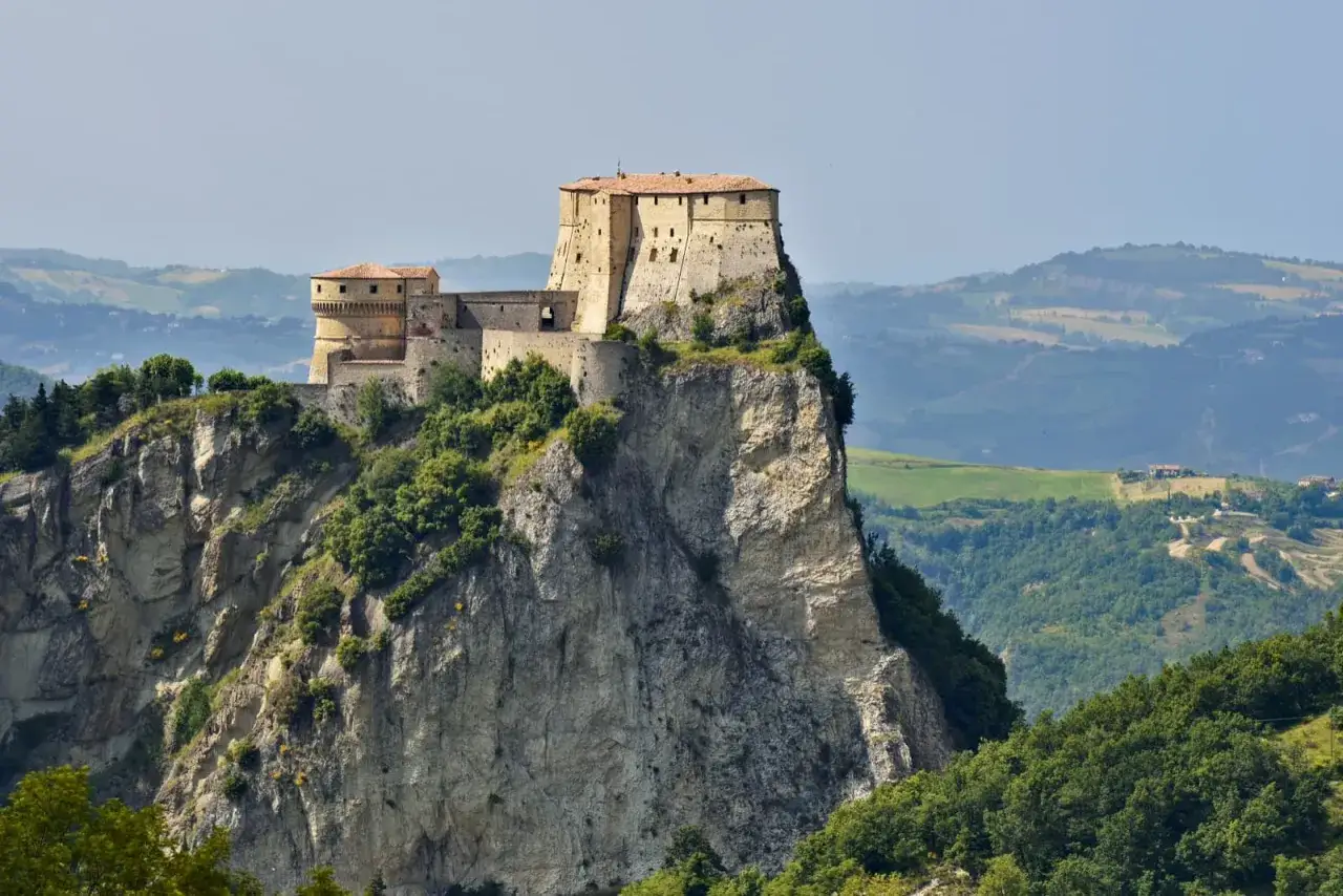 Rocche imponenti e borghi medievali in Emilia Romagna, arroccati su speroni rocciosi, dominano paesaggi collinari verdi.