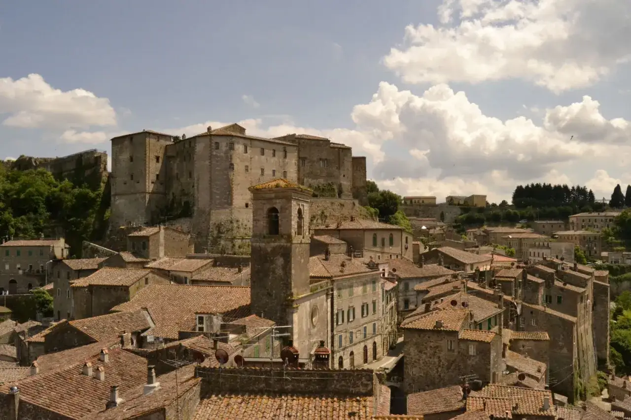 Panoramica di antichi borghi vicino Follonica, con un imponente castello in cima alla collina e un campanile che svetta tra i tetti rossi.