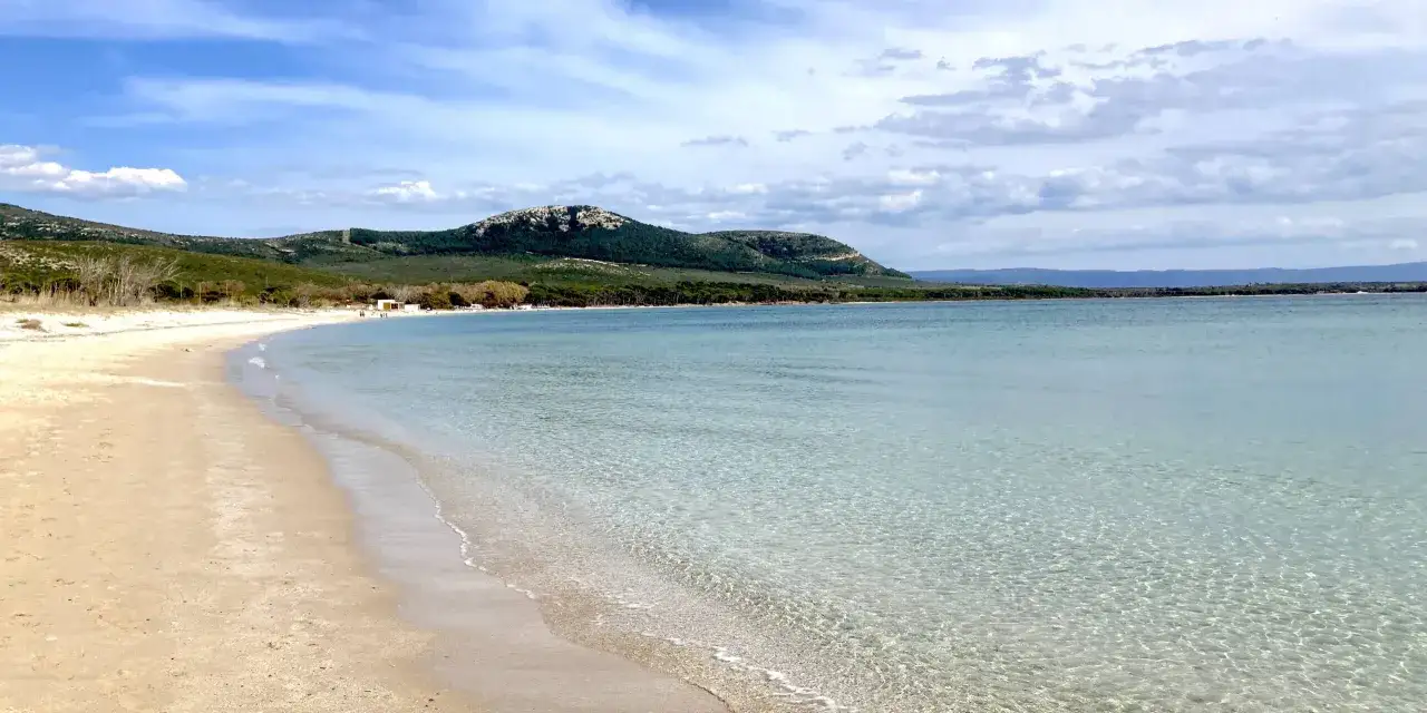 Spiagge alghero e dintorni: sabbia dorata, mare cristallino e colline verdi sotto un cielo azzurro con nuvole bianche.