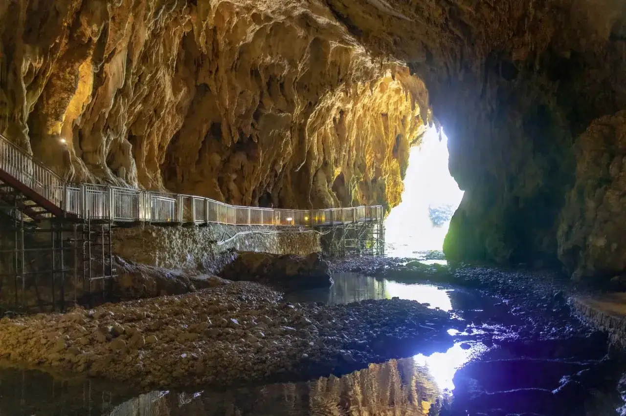 Sentiero illuminato tra le stalattiti dorate delle grotte di Pastena, con un ruscello che riflette la luce.