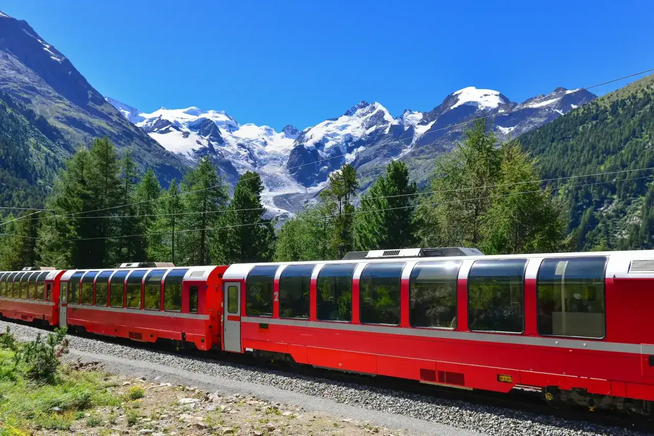Il trenino del Bernina, con le sue iconiche carrozze rosse, attraversa un paesaggio alpino mozzafiato, pronto a partire verso vette innevate.