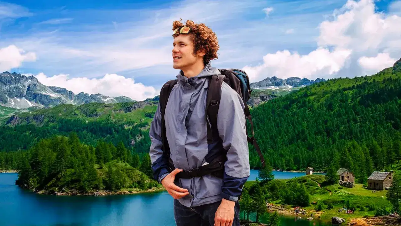 Giovane escursionista ammira un lago alpino in una splendida località montagna Piemonte, con boschi e cime innevate sullo sfondo.