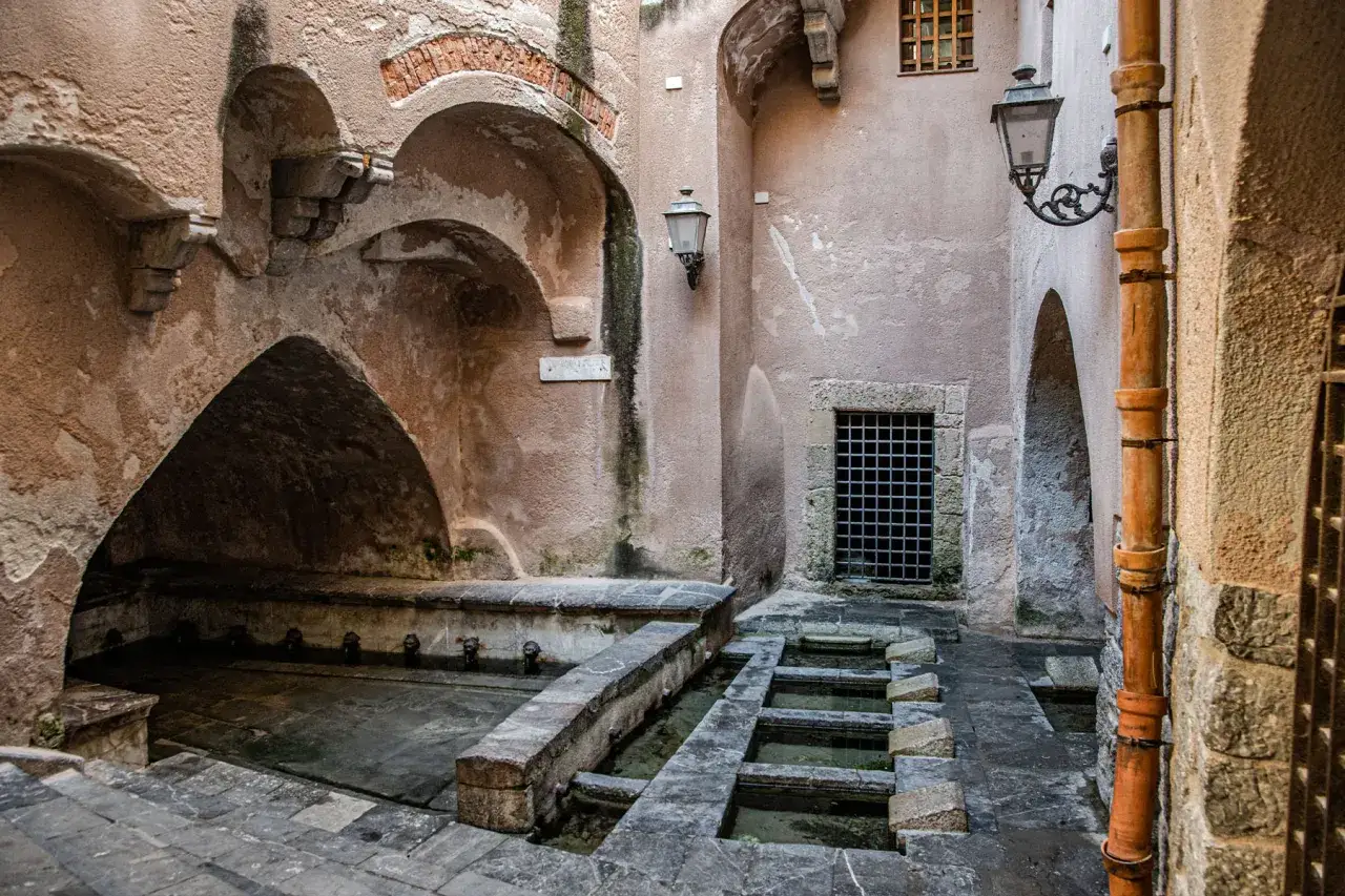 Antica lavanderia nel borgo Cefal&ugrave; centro storico, con archi in pietra e rubinetti a forma di leone.