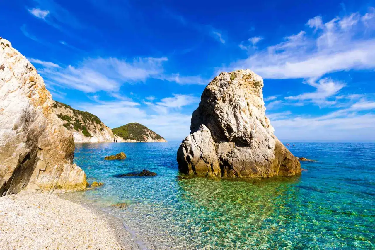 Scogliera imponente su un mare cristallino, un angolo di paradiso che sembra vicino a Firenze, con isole verdi all'orizzonte.