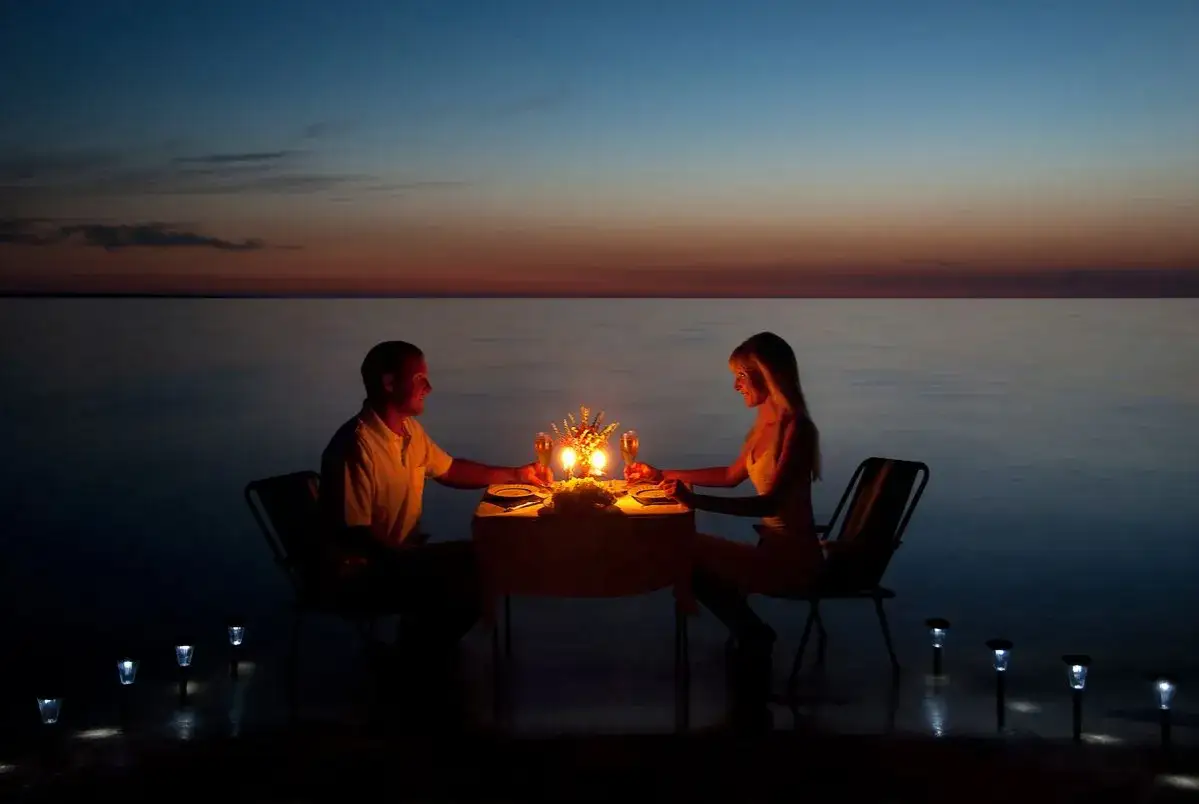 Una coppia al mare di sera, cena romantica a lume di candela con vista sull'oceano al tramonto.