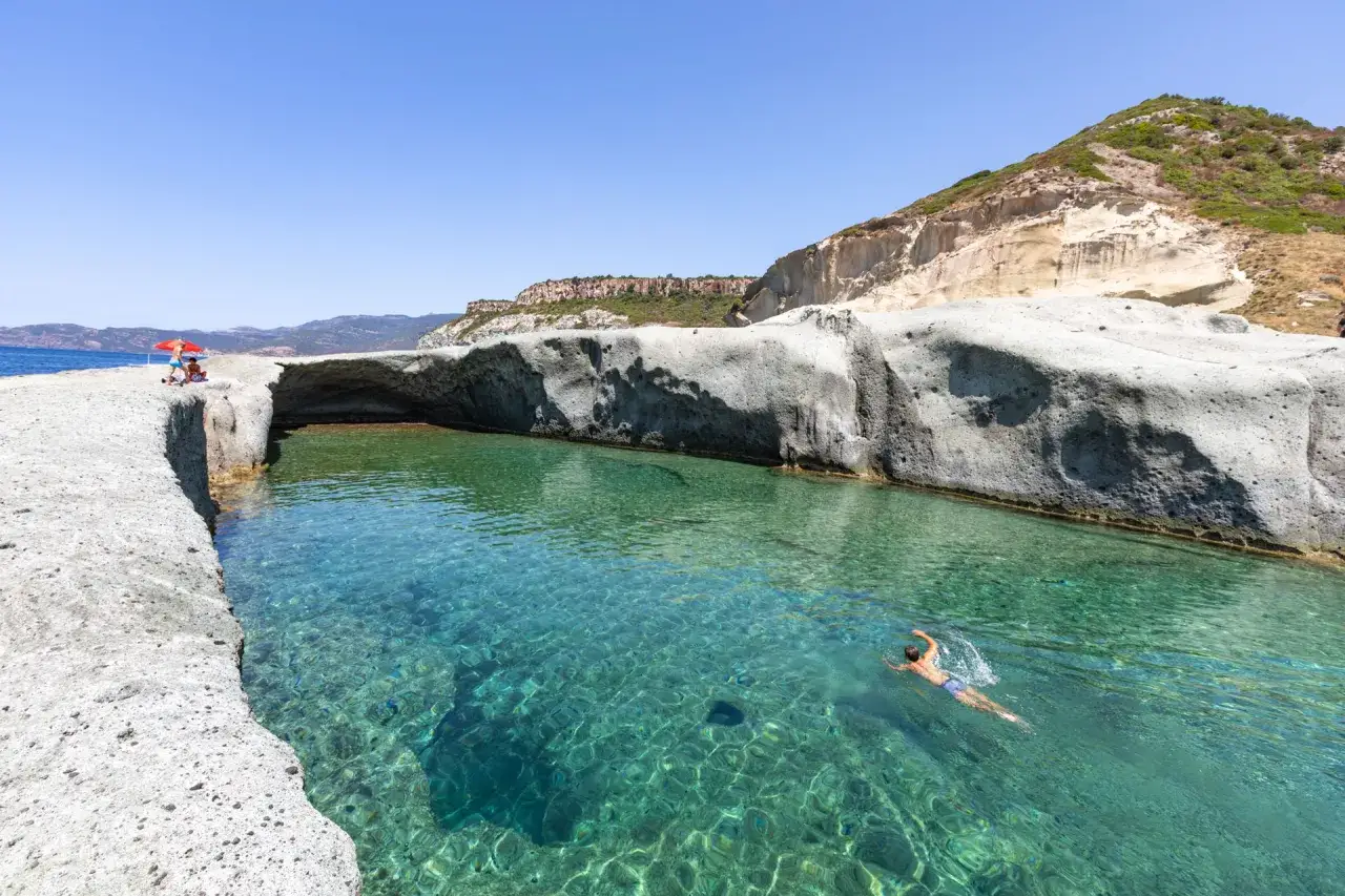 Un uomo nuota in acque cristalline tra scogliere bianche. Un luogo ideale per scoprire le spiagge di Bosa e cosa vedere.