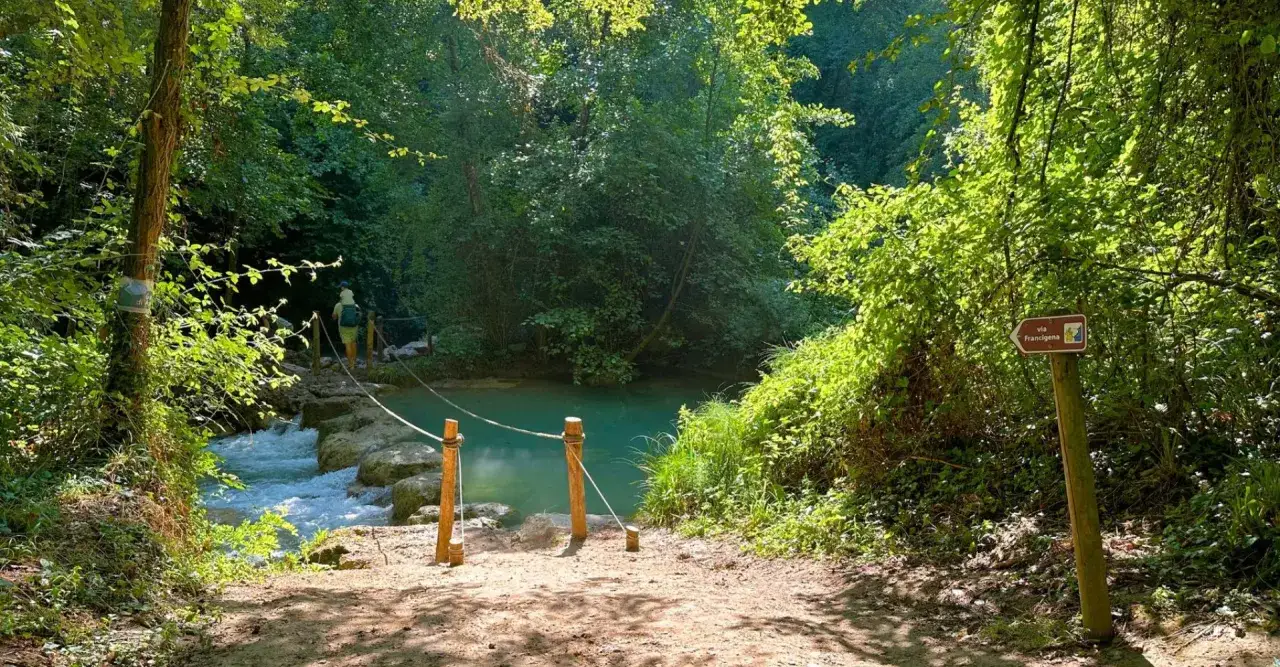 Sentiero in Toscana con guado su fiume turchese. Segnale Via Francigena indica i percorsi a piedi.