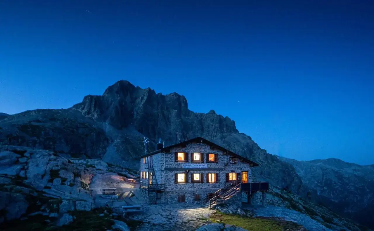 Rifugio Tita Secchi, uno dei rifugi Val Camonica facili, illuminato di notte con montagne imponenti sullo sfondo.