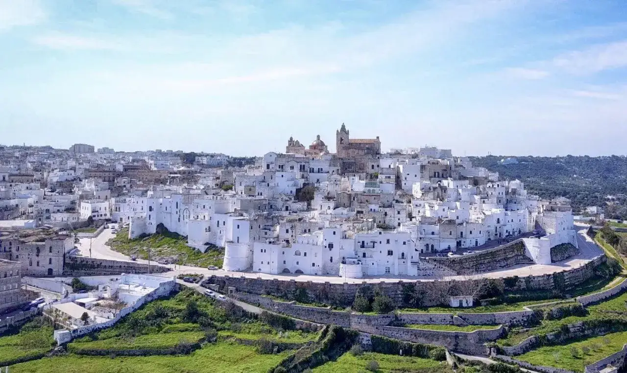 Un incantevole panorama di borghi medievali in Puglia, con case bianche arroccate su una collina sotto un cielo azzurro.