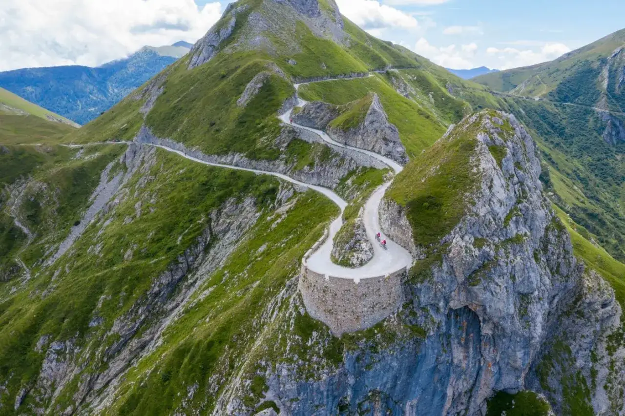 Ciclisti affrontano tornanti mozzafiato sul via del sale cammino, un percorso spettacolare tra montagne verdi e rocce imponenti.