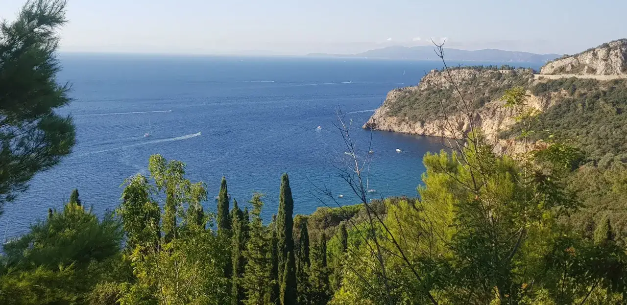 Vista panoramica del mare blu con barche a vela e gommoni, scogliere rocciose e vegetazione mediterranea. Per raggiungere la cala, Argentario, si può ammirare questo splendido paesaggio.