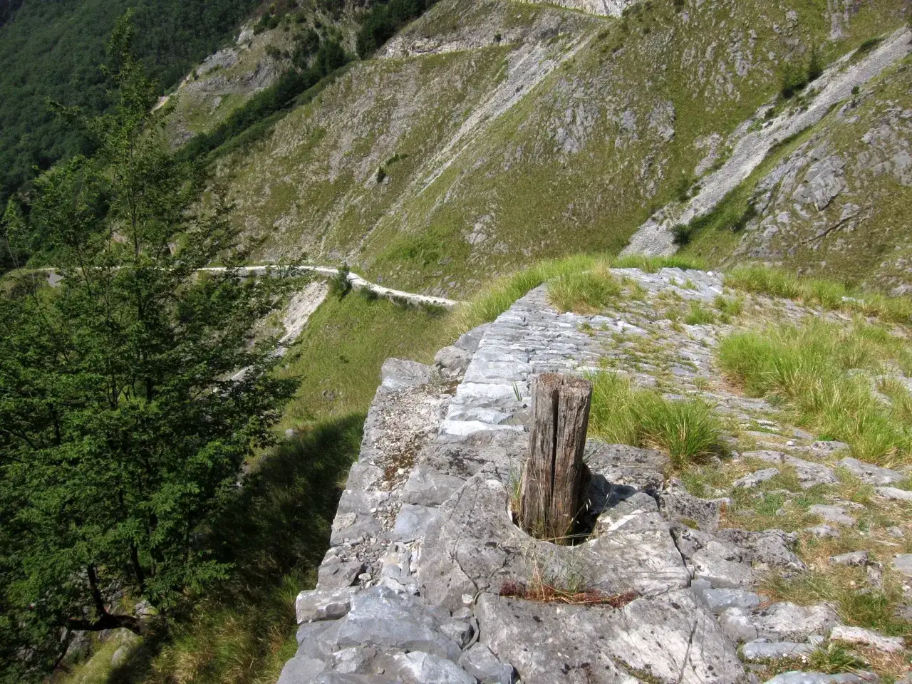 Sentiero lastricato su un versante montuoso, con un tronco di legno. Un tratto della via Vandelli, ideale per le tappe di un trekking.