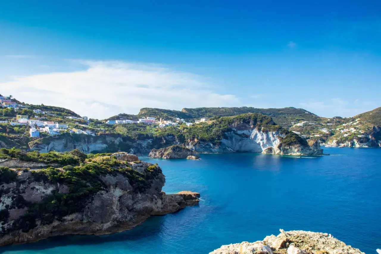 Panorami mozzafiato della cala dell'acqua a Ponza, con case colorate aggrappate alle colline verdi e un mare azzurro intenso.