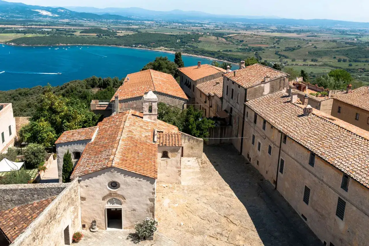 Vista dall'alto del populonia centro storico, con case dai tetti rossi e il mare blu sullo sfondo.
