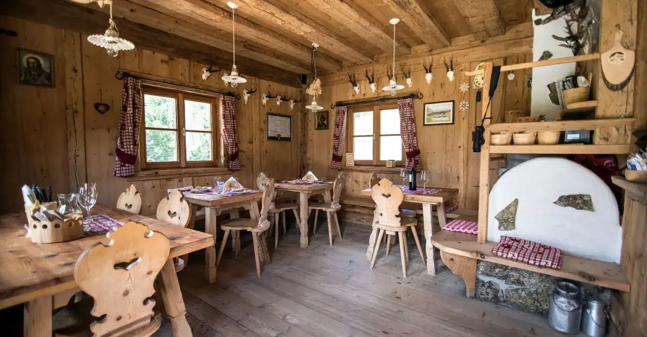 Interno accogliente di una malga in Alto Adige, con tavoli in legno, sedie intagliate e decorazioni alpine.