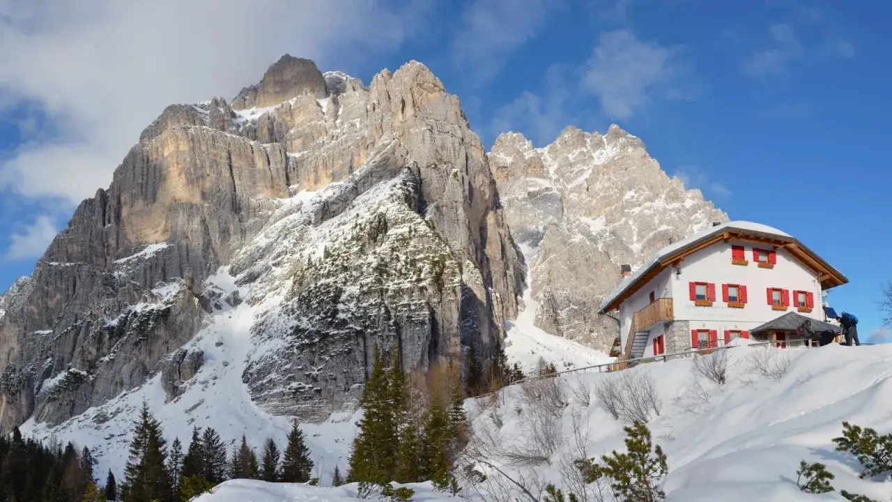 Rifugio alpino con tetto rosso e finestre, incastonato tra imponenti vette innevate. Un vero gioiello tra i posti belli in montagna Veneto inverno.