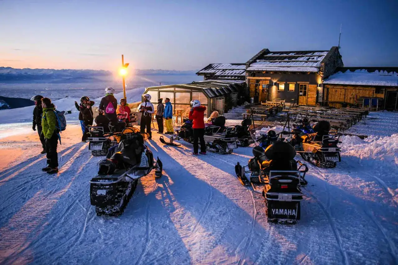 Gruppo di persone con motoslitte davanti a un rifugio in montagna, pronti per festeggiare il capodanno in rifugio Piemonte.