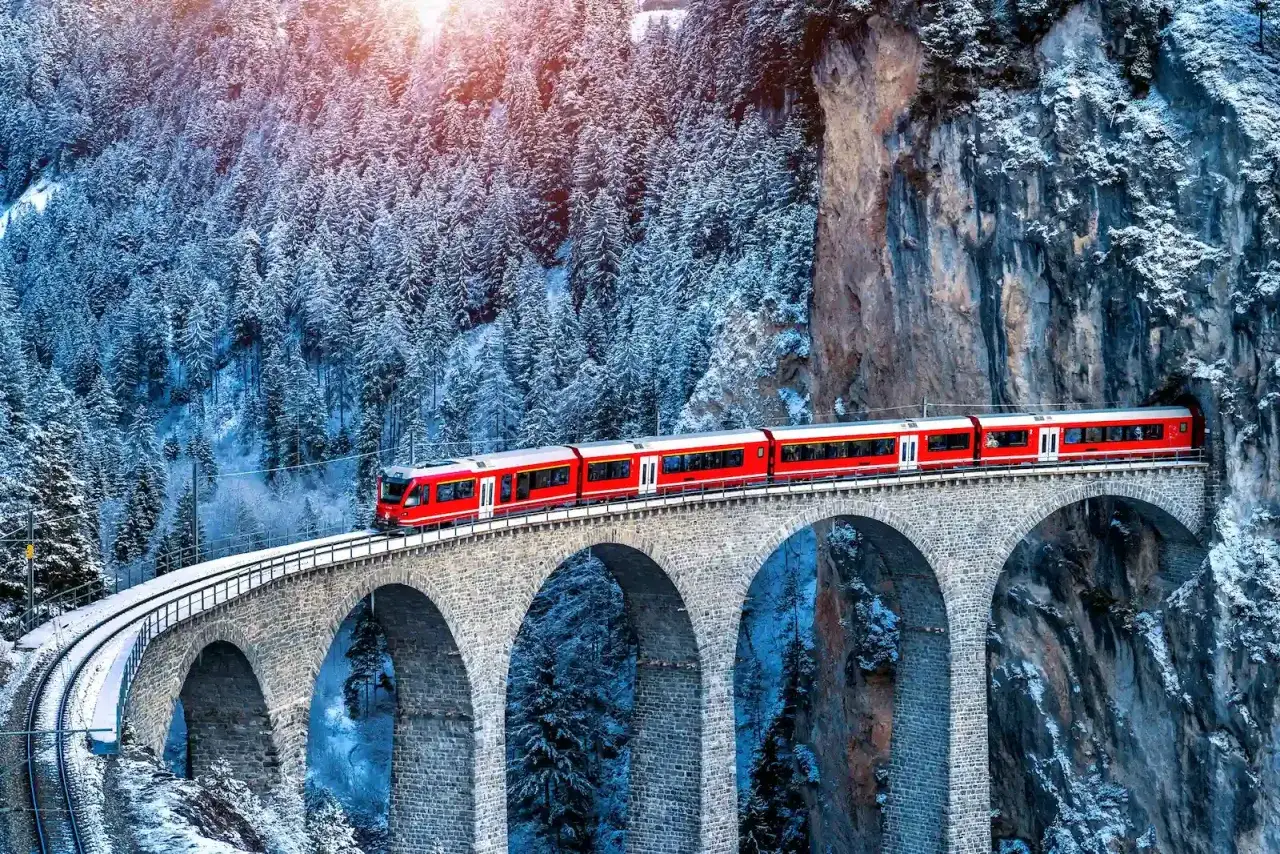 Il trenino del Bernina attraversa un viadotto innevato, immerso in un paesaggio alpino mozzafiato.